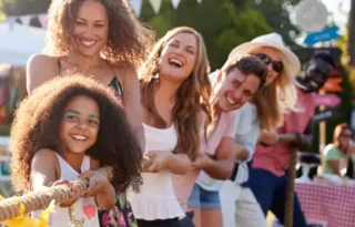 Group of people pulling rope in tug-of-war at an outdoor charity fundraising event.