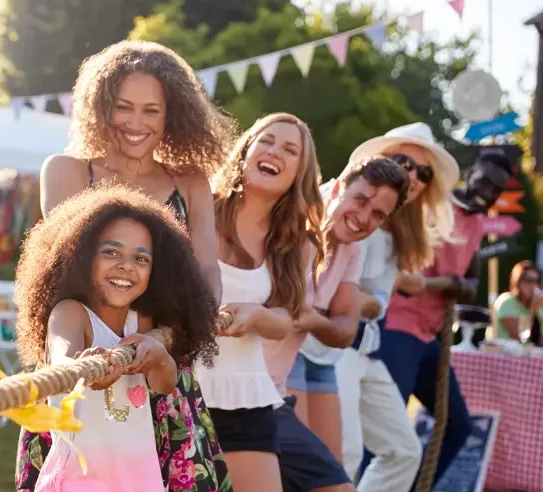 Group of people pulling rope in tug-of-war at an outdoor charity fundraising event.